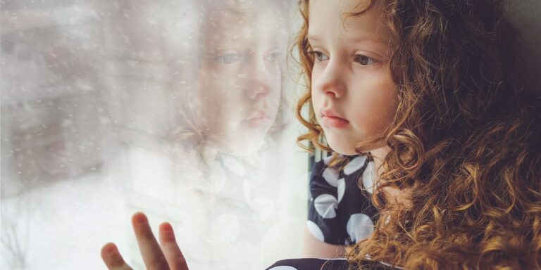 little girl looking out at the snow thru the window